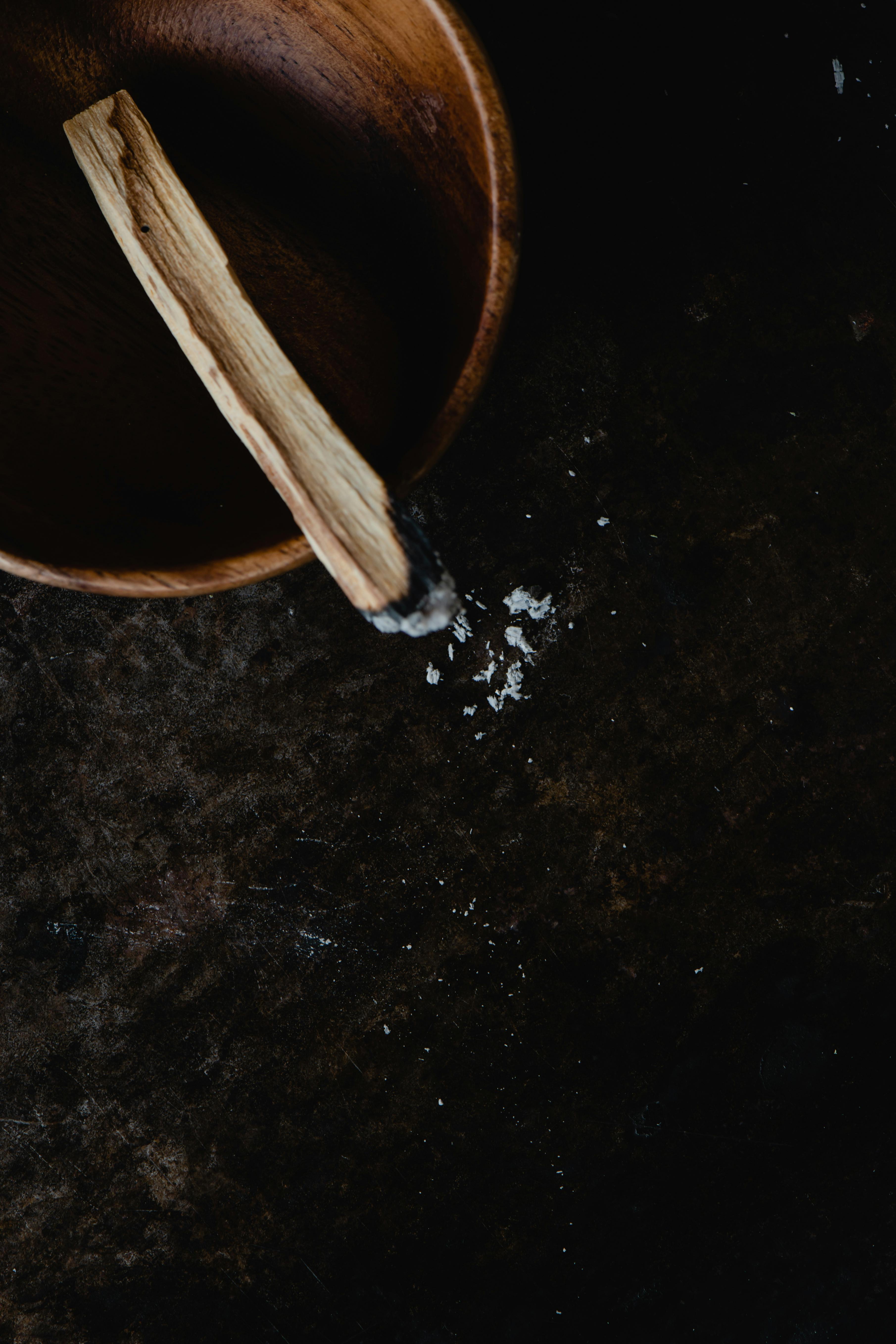 Burnt palo santo stick resting on a wooden bowl with a little ash on the tray