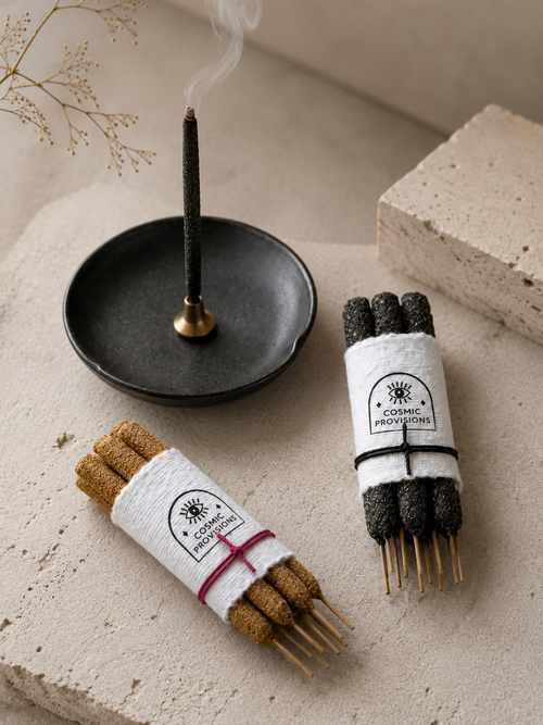 Copal incense stick burning in brass holder sitting on black ceramic tray shown with handrolled incense bundles — Cosmic Provisions