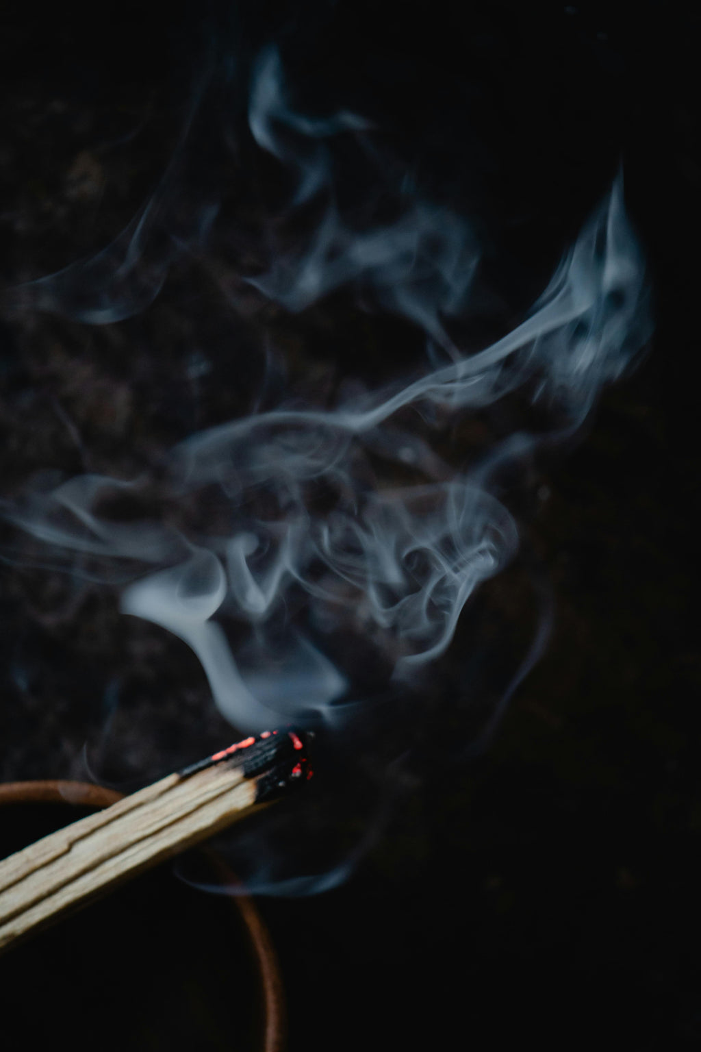 Palo Santo lit with smoke rising against a dark background